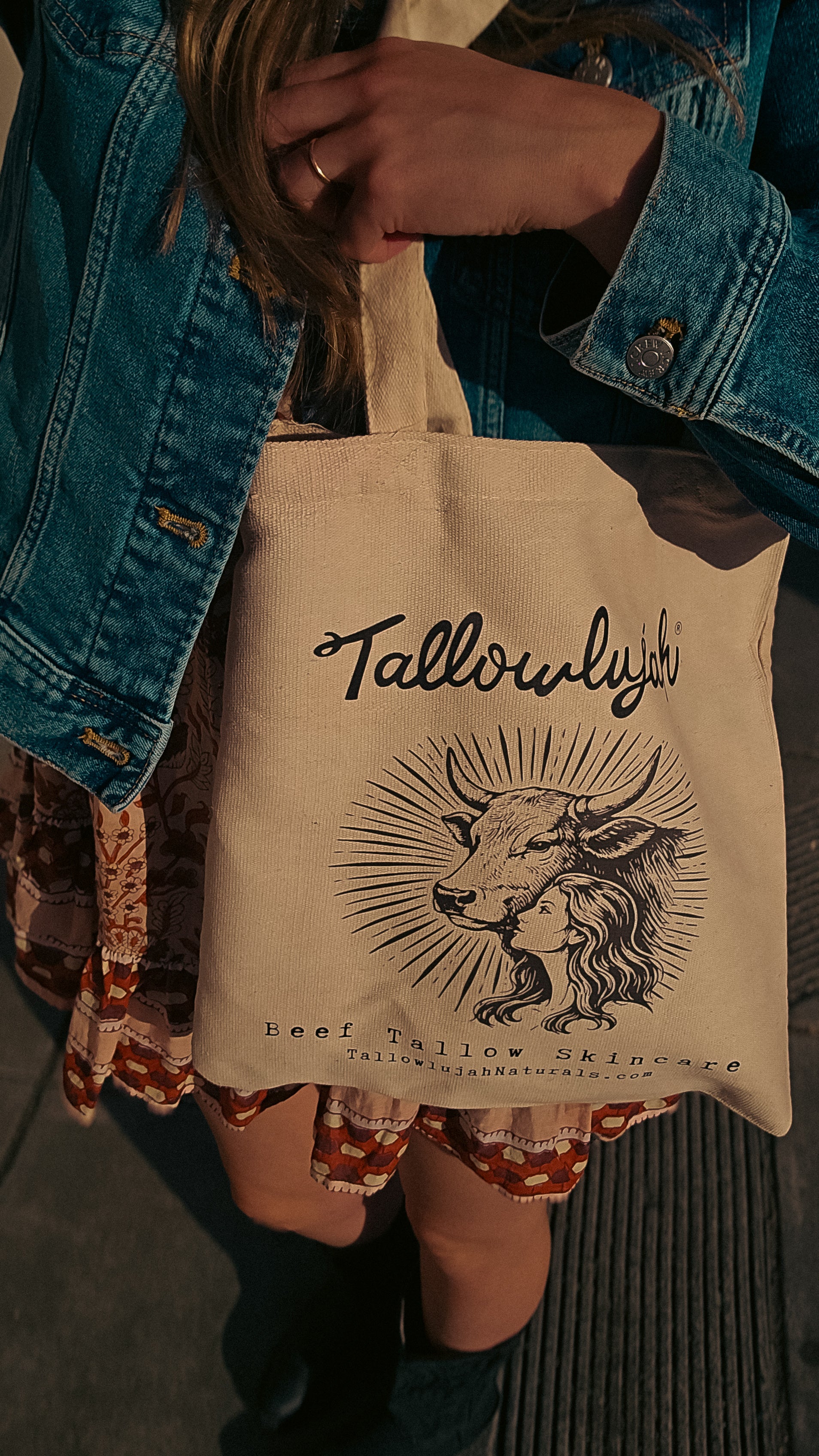 Person holding a tote bag with 'Tallowlight' branding and cow illustration.
